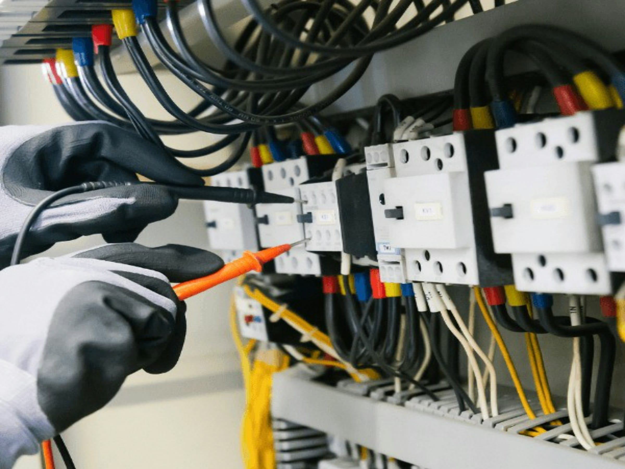Gloved hands testing an electrical panel with a multimeter