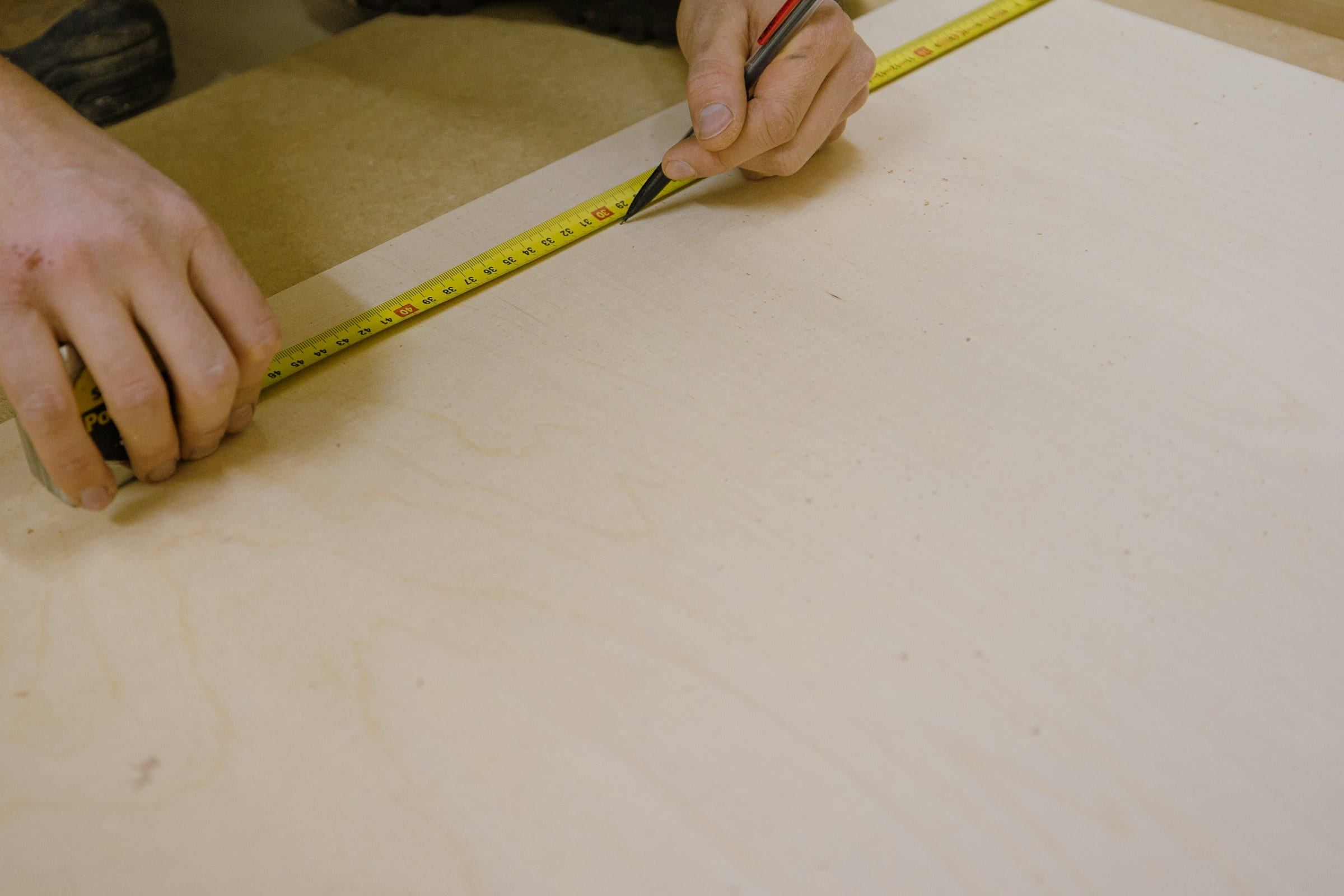 Hands measuring and marking a panel with a tape measure and pencil