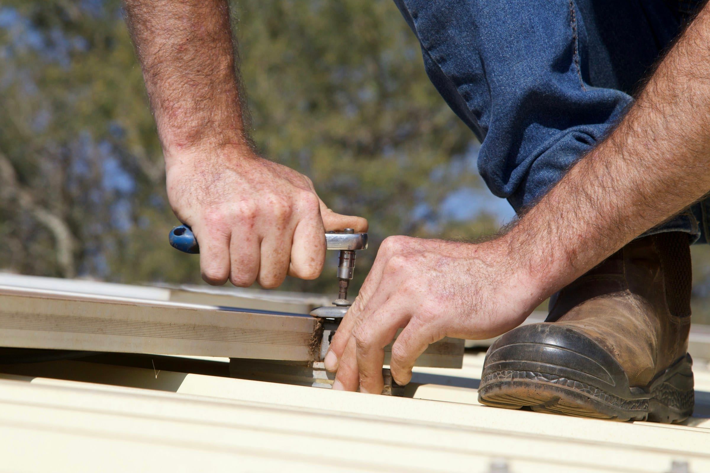 Hands fastening metal roof panels with a socket wrench